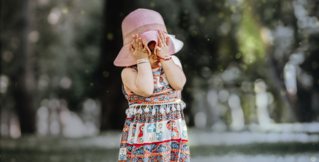A young girl in a hat covers her face