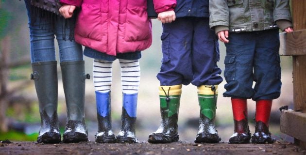 Four children wearing raincoats and rain boots standing in a row.
