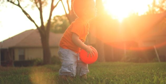 Child playing with orange balloon, sun setting behind him.