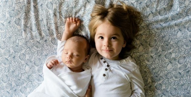 little girl and baby laying in bed