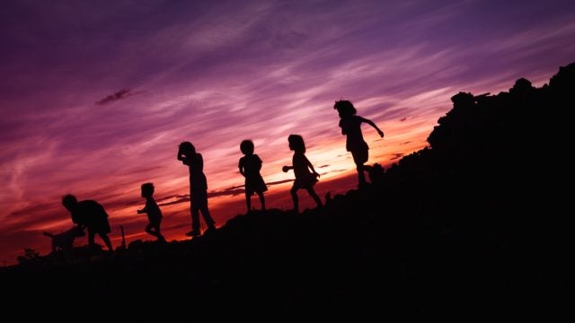 Children playing are silhouetted against a sunset.