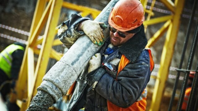 A construction worker carries a heavy pipe