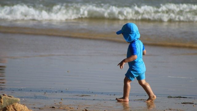 A child in a sun hat walks along the beach on a hot day