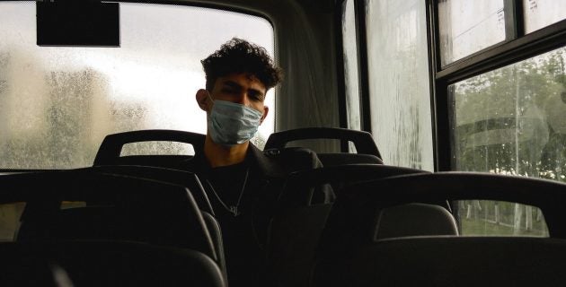 Man in a facemask sits on a bus while it pours outside