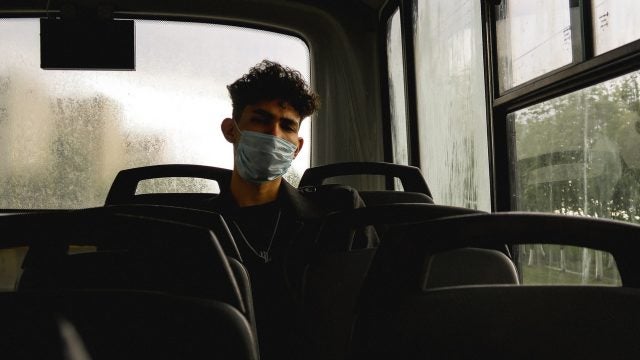 Man in a facemask sits on a bus while it pours outside