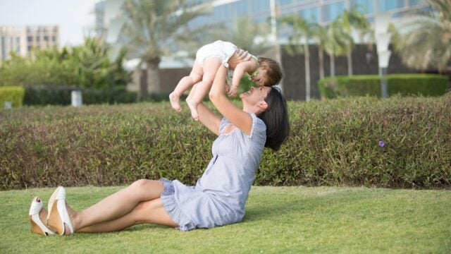 A woman lifts a baby while sitting in the grass.