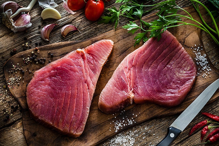 Raw tuna steak on a cutting board with garlic and tomatoes.