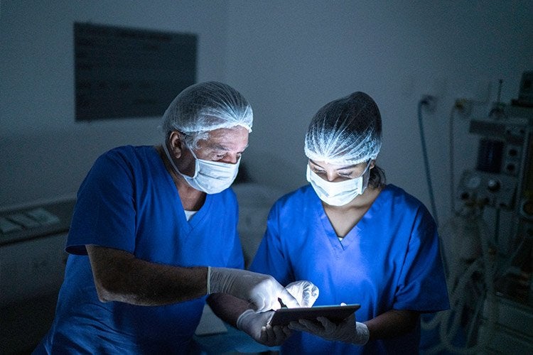 Doctors wearing masks looking at tablet to assist during surgery