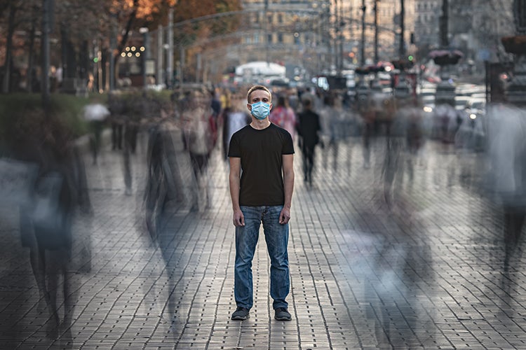 The young man with medical face mask stands on the crowded street