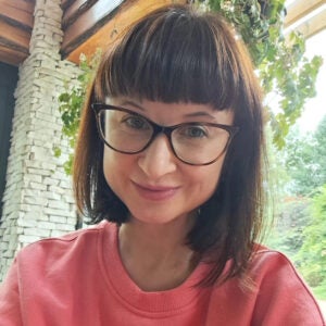 Tetiana Matviiuk wearing a pink sweater outside, in front of a leafy, green plant.