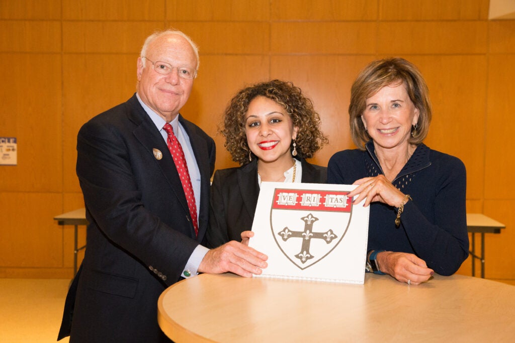 A donor couple and a student pose together with the Harvard Chan crest