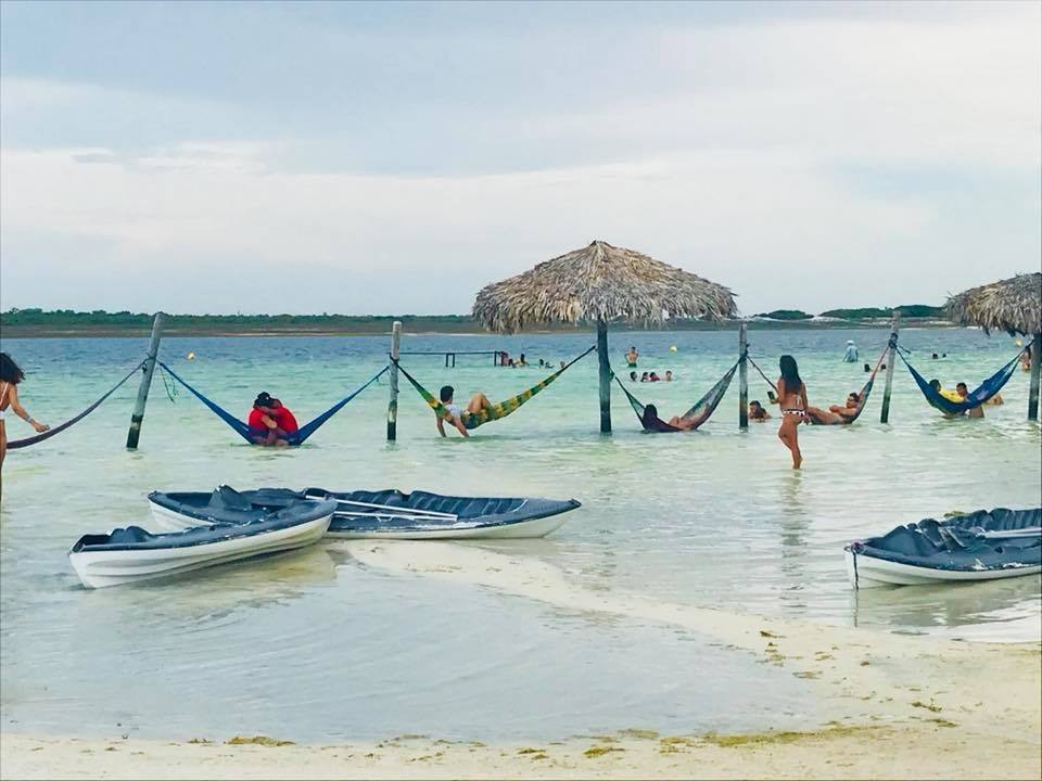 beach photo with boats and people in hammocks in water
