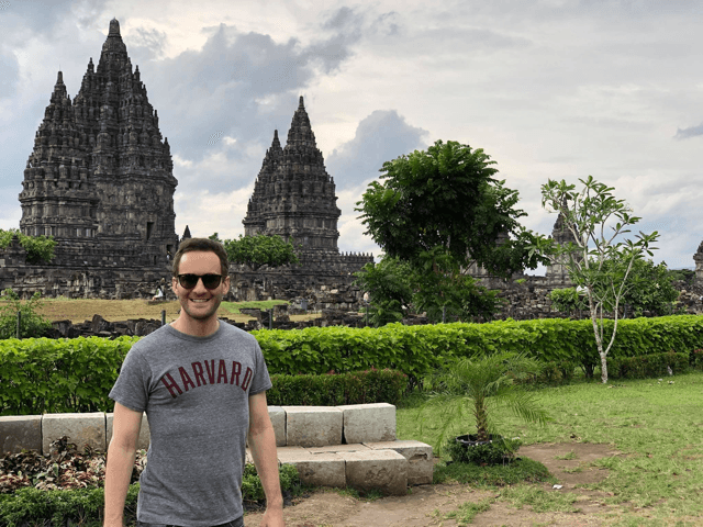 student in Harvard t-shirt posing in front of Prambanan Temple in Yogyakarta, Indonesia