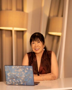 Phyllis Kanki sitting before her laptop in a brown dress.