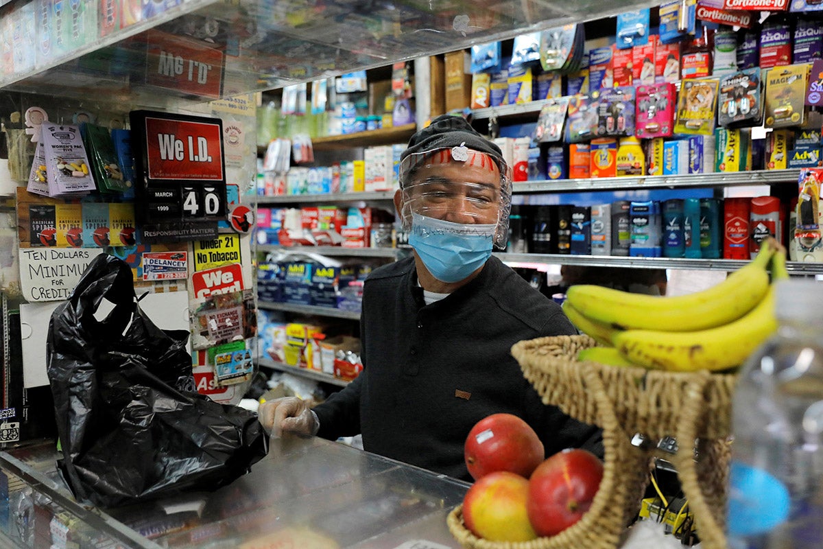 A store clerk pictured behind the counter with a mask and face shield made from a gallon water jug