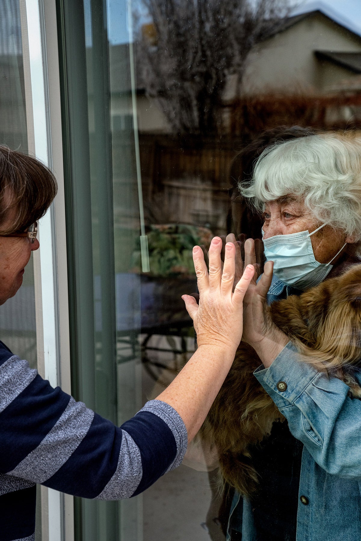 Woman touches hands with an elderly woman through a glass window