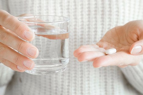 Woman's hands holding a glass of water and white pill. Receiving vitamins. Medical, pharmacy and healthcare concept.
