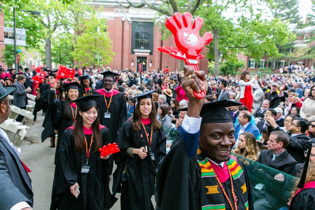 Students at commencement in Cambridge holding "wash hands" sign