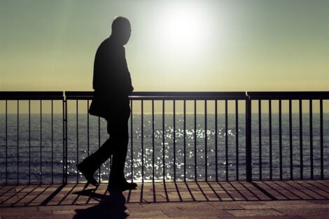 A dark silhouette of an unrecognizable man walking along a beach promenade in summer sunrise