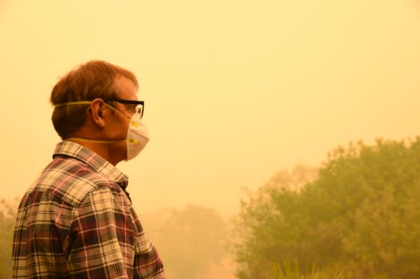 A man wears a face mask to protect himself against very dangerous level of air pollution. A thick yellow fog coming from the nearby forest fires covers Canberra city.