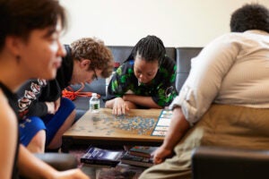 Staff and clients at a GLASS drop-in space for youth sit around a table working on a puzzle.