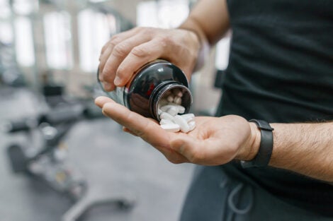 Close up of a man's hands taking supplement pills, with gym equipment in background