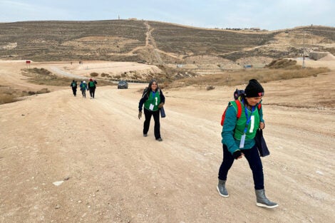 Students wearing green vests walk on a road in a desert environment.