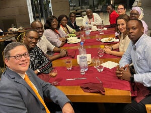 A group of Senegalese health care researchers and Tim Rebecck pose for the camera at a group dinner. The table has a red tablecloth. 