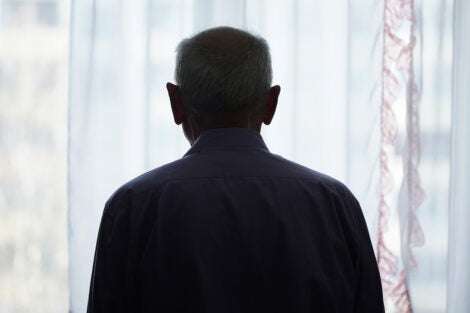 Silhouette of older man looking through window with transparent curtain. Rear view.