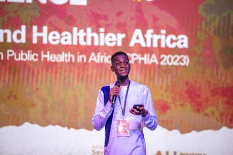 Esias Bedingar speaking in front of a banner reading "Healthier Africa"