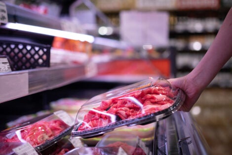 Hand of a person picking up a container of meat at a grocery store