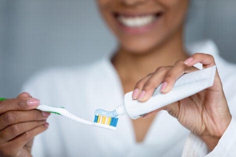 Close up young smiling woman applying whitening paste on toothbrush, doing toothcare procedures at home, taking care of gums health, preventing caries, healthy daily habit concept.