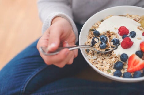 Person eating a bowl of granola, fruit, and yogurt