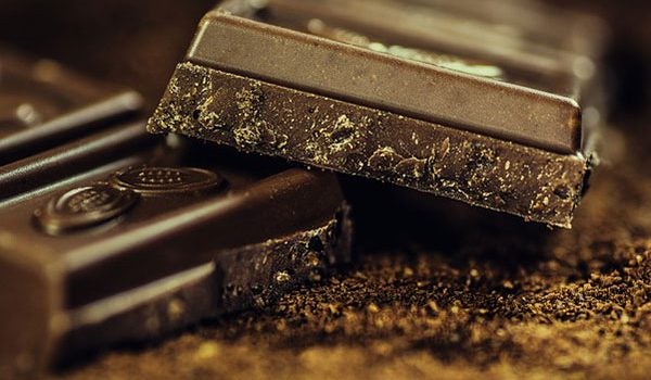 Two squares of dark chocolate resting on dark chocolate shavings