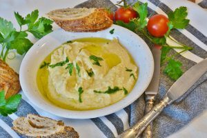 bowl of hummus on table with bread, tomatoes, and parsley