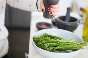 broccolini in a bowl with person adding pepper