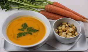 bowl of carrot and coriander soup with carrots and dish of croutons on tray