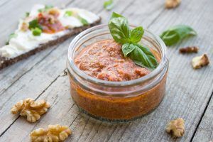 small dish of muhammara on a table with walnuts and flatbread