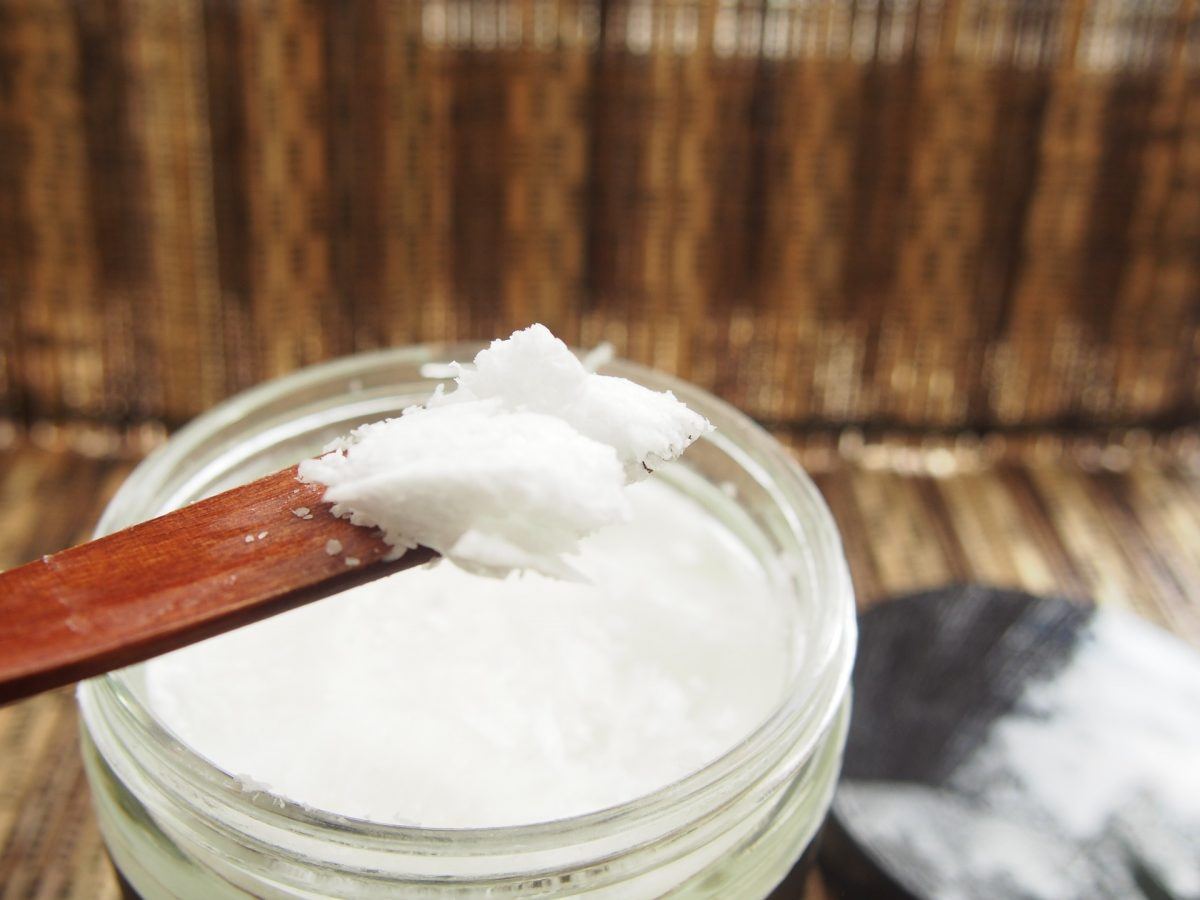 wooden spoon scooping out coconut oil from a jar