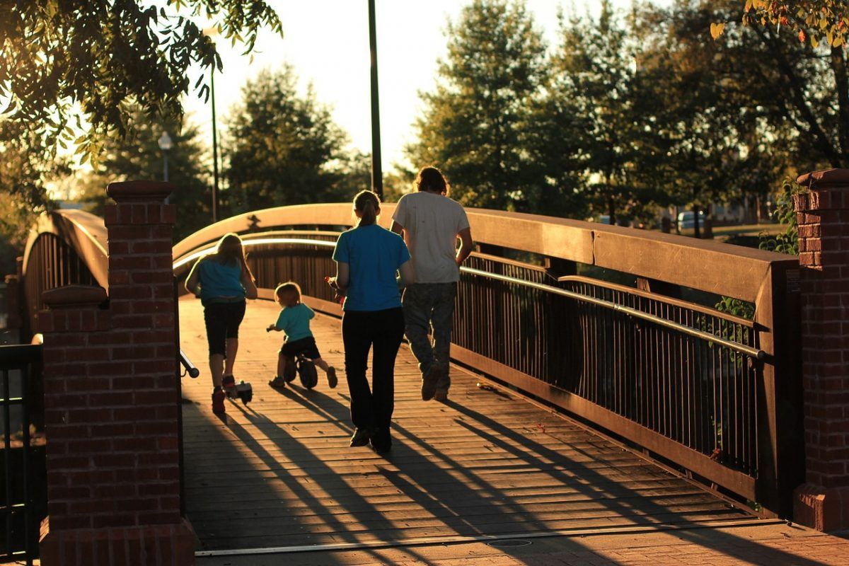 family walking over a bridge wth kids on a tricycle