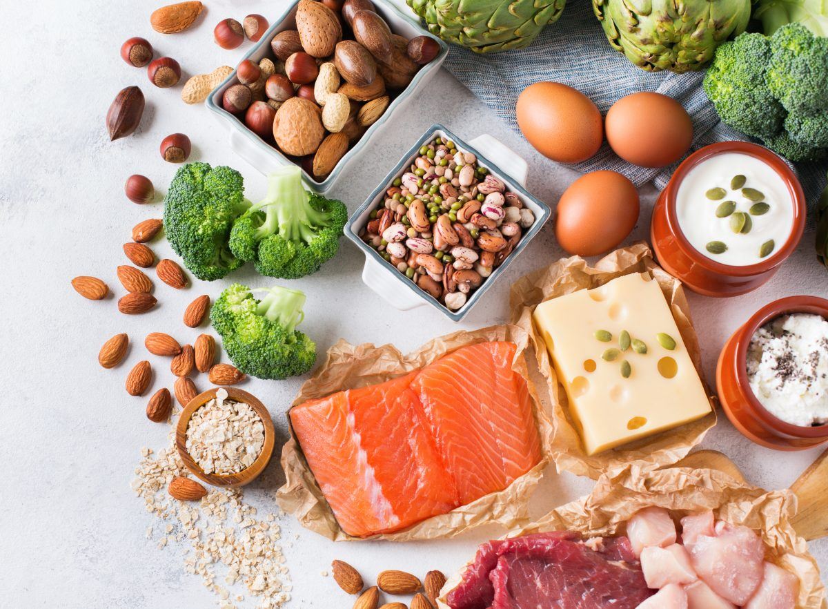 A variety of protein foods, including egg, salmon, beef, chicken, beans, lentils, almonds, quinoa, oats, broccoli, artichokes, yogurt, cheese, and tofu