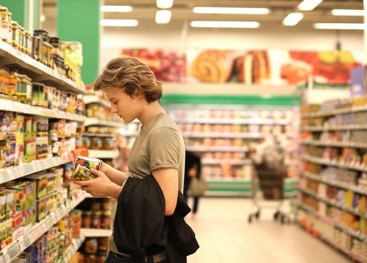 Man reading the labels to compare two jarred products while standing in a supermarket aisle
