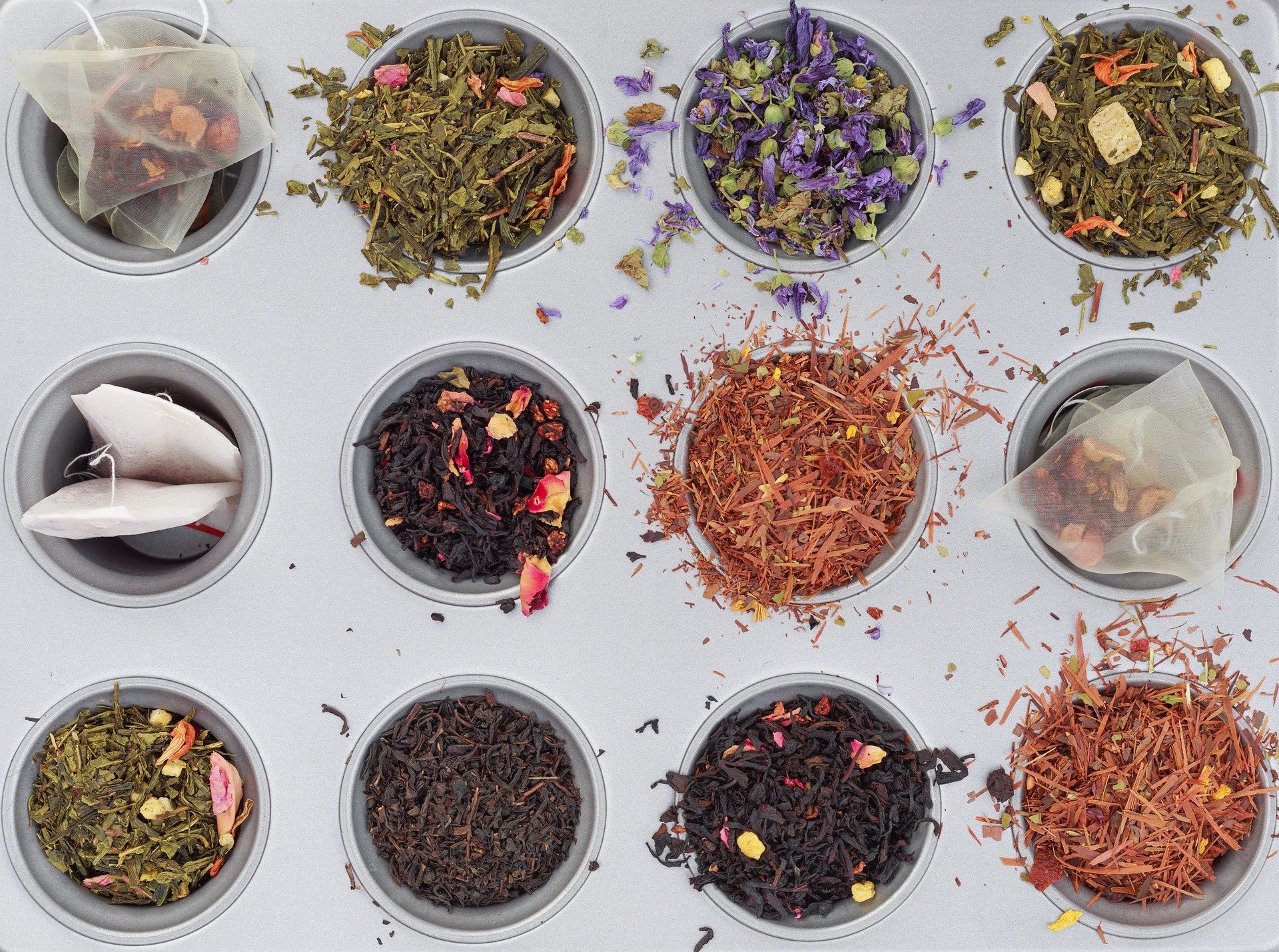 A variety of loose leaf and bagged teas in cups of a baking tray