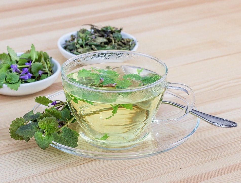 a glass teacup filled with herbal tea made of mint leaves and other herbs and flours in bowls alongside it
