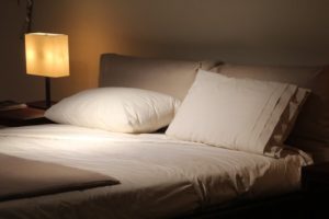 Bed with white sheets and pillow in a dimly lit, calm room for sleeping