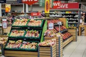 photo of a supermarket aisle with sale signs over the produce section filled with apples