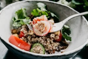 a fork in a dinner bowl of quinoa, salad, radishes, cucumbers
