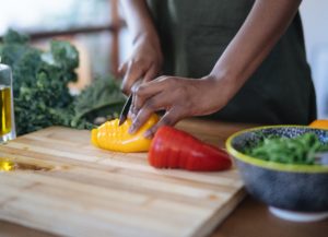 woman chopping yellow and red peppers on a bamboo cutting board alongside a chopped bowl of kale