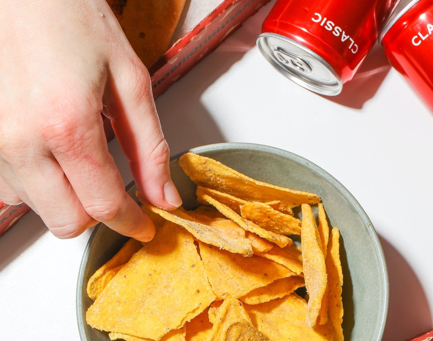 hand reaching into chips in a bowl, with cans of cola on the side