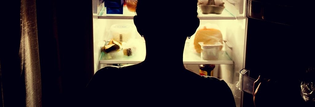 A sillhoutte of a person backlit by the light of a refrigerator, looking for something to eat
